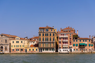Colorful historic buildings along Venice canal. Close-up view of vibrant old Venetian buildings with balconies and shutters lining the canal under a clear blue summer sky.