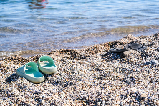 Two pairs of flip flops on a pebble beach with ocean water. Summer holiday shoes by the sea shore in Turkey.