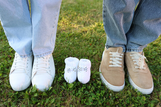 Couple’s shoes on grass with tiny baby booties in middle, creative pregnancy announcement family photo.
