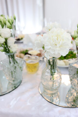Glass vases with white carnations and lisianthus on wedding table, elegant floral centerpiece decor.