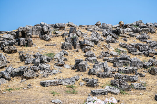 Ancient ruins of Hierapolis in Turkey under a clear blue sky. Historic stone blocks scattered on dry grass, archaeological site. - Powered by Adobe