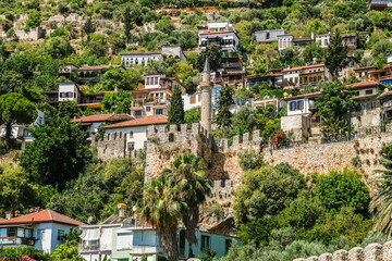 Obraz premium A vibrant overview of the historic Alanya castle complex and traditional houses on a lush green hillside in Turkey.