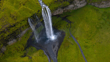 Seljalandsfoss waterfall in Iceland cascades from a tall cliff into a shallow pool, surrounded by green moss, grass, and a curving walking path.
