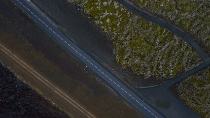 A straight paved road divides moss covered volcanic terrain and barren ground in Iceland, showcasing contrasting textures and rugged landscapes.