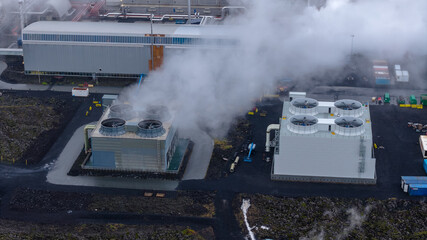Geothermal power plant in Iceland with two cooling towers emitting steam, surrounded by dark...