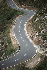Scenic winding mountain road with sharp curves, safety barriers, and road signs surrounded by rocky hillside and sparse vegetation, symbolizing adventure, travel, and challenge; telephoto shot