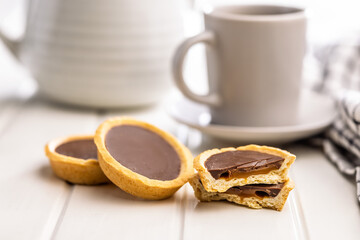 Sweet chocolate tartelettes and coffee cup on white table.