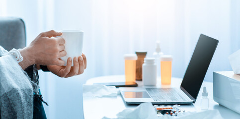 Young unrecognizable guy having fever wrapped in blanket and drinking hot tea, sitting on sofa and watching film on laptop, side view, panorama with free space