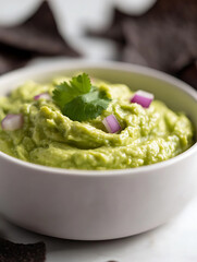 Obraz premium Creamy avocado dip, garnished with cilantro and red onion. Perfect for dipping! Served in a simple white bowl and paired with dark chips.