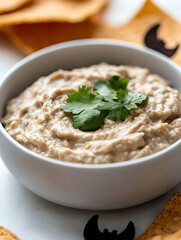Creamy dip in a white bowl, garnished with cilantro. Surrounded by chips and festive Halloween decor. Perfect snack for a party or casual gathering.