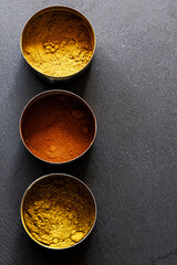 Three metal containers in a row with spices, on a slate background