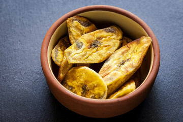 Crispy plantain chips in clay bowl on dark background