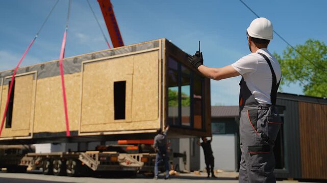 Construction worker directing crane lifting prefabricated modular house