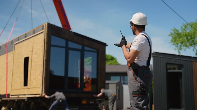 Construction worker directing crane lifting prefabricated tiny house module