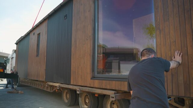 Construction worker checking stability of prefabricated tiny house on truck
