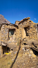 Fototapeta premium An abandoned stone house with a weathered door and dry grass reflects rural decay and the passage of time in a quiet mountainous landscape. 📍Bolbar village, Hawraman Takht 