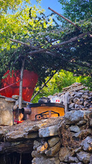 Rustic stone shelter nestled in a garden among trees, shaded by branches and blending traditional craftsmanship with natural greenery.  
📍Masrachi, Kamalla 