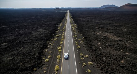 Fototapeta premium Car on desolate road through volcanic terrain under vast sky