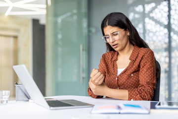 Office worker suffering from wrist pain while working on laptop