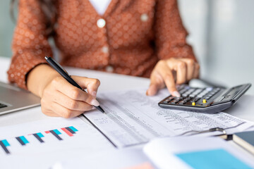Fototapeta premium Accountant using calculator and taking notes while analyzing financial data