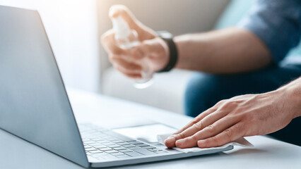 Device disinfection. Male hand using disinfectant spray and cloth for cleaning laptop keyboard while working from home during coronavirus pandemic, crop, closeup