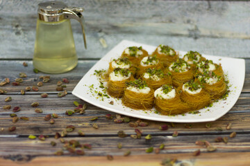 Osh el Bulbul Pastries topping with Cream and Pistachios in plate on wooden table side view of Middle Eastern dessert