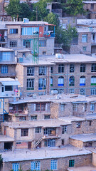 Stone village with flat-roofed homes and colorful windows, surrounded by greenery and sunlight,...