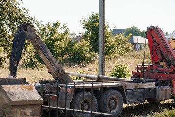 Red Crane Truck Loading Timber on Rural Roadside, Construction Scene, Sunny Day, Green Trees, Orange Machinery, Industrial Equipment, Exterior Shot.
