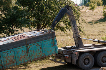 Demolition Waste Removal: Blue Dumpster Truck Lifting Debris with Crane Arm in Rural Field Environment, Rustic Texture.