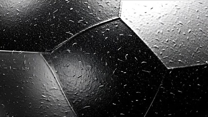 Close-up of a dark polygonal sports ball surface covered in numerous small irregularly shaped water droplets and textured bumps