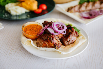 Grilled pork kebab with fresh herbs, red onion, lavash and spicy red pepper sauce