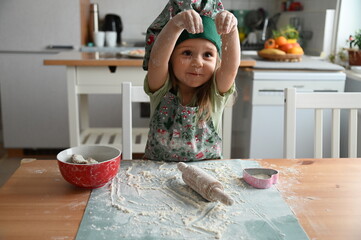 Cute smiling toddler girl in chef hat playing with dough for Christmas baking