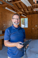 A home inspector smiling at the camera in a workshop holding an iPad for inspecting