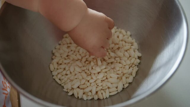 Close-up of a baby's hand reaching into a bowl of puffed rice cereal, a fun moment of food preparation and baking for Christmas with mom or dad