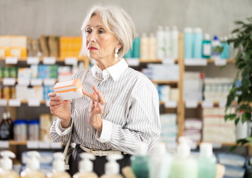 Mature woman holds packages of paracetamol in her hands against the background of shelves with pharmacy products and medicines. Pensioner buys headache pills at a pharmacy