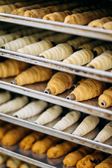 Assortment of croissants, eclairs, and pastry tubes on metal trays in bakery kitchen