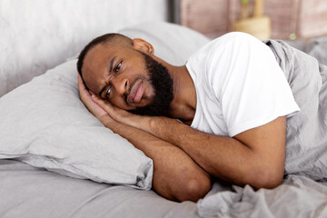 Depression Concept. Portrait of upset African American man lying in bed in the morning and thinking. Sad black male feeling lonely or stressed, suffering from lack of sleep, distraught