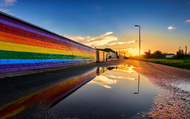 Obraz premium Vibrant Rainbow Mural Reflected in Puddle at Sunset
