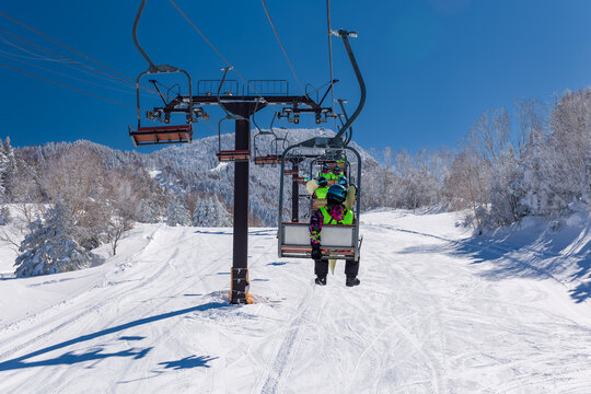 First person view from a ski chair lift with snowboarders ahead on a sunny day in Japan.