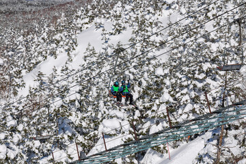 High angle view of a ski lift carrying two people over a dense winter forest scene