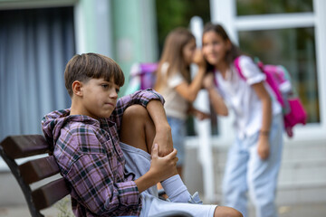 Boy sitting on bench while girls whisper nearby