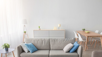 Nobody in apartment, minimalist style and modern blog about interior. Gray sofa with colored pillows, armchair, carpet, table, window with curtain on light wall background, in scandinavian living room
