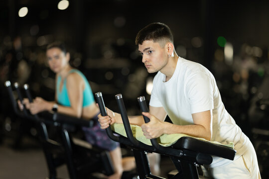 Focused young man performing hamstring exercise on standing leg curl machine in modern gym environment, building lower body strength