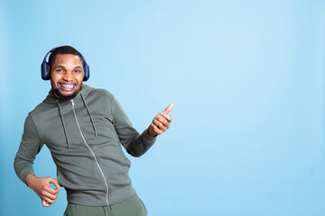 Naklejka premium African american funky guy playing air guitar and listening to music, having fun with his new rock and roll playlist against blue background. Cheerful young man with lively rhythm.