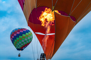 Colorful hot air balloons with fire burner flame filling envelope against blue sky, adventure travel concept, festival of aerostat flight with vibrant colors and dramatic fire