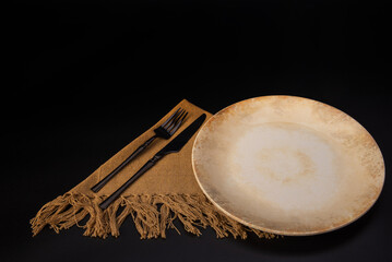 Beautiful table setting, beautiful plate, cutlery and napkin placed on a dark background, selective focus.