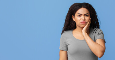 Aching teeth. Unhappy black lady suffering from toothache pain touching cheek, posing over blue...