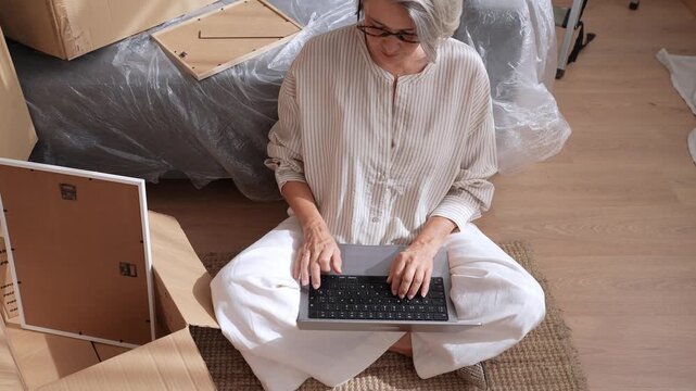 Woman working on laptop surrounded by moving boxes