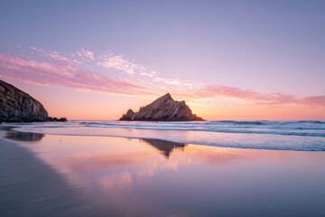capture breathtaking sunset over tranquil beach featuring solitary rock rising from sea