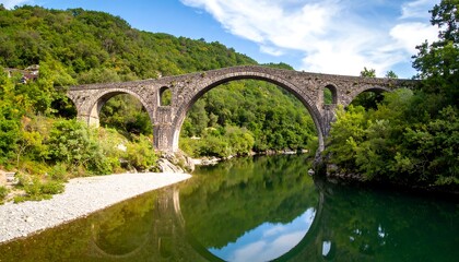 Fototapeta premium Ancient stone bridge over the river with reflections in the water under blue sky